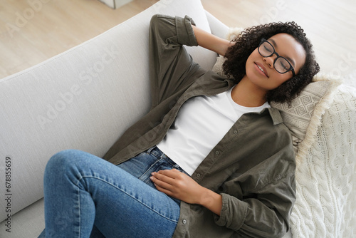 Relaxed serene young mixed race girl resting lying on comfortable sofa, enjoy afternoon nap at home photo
