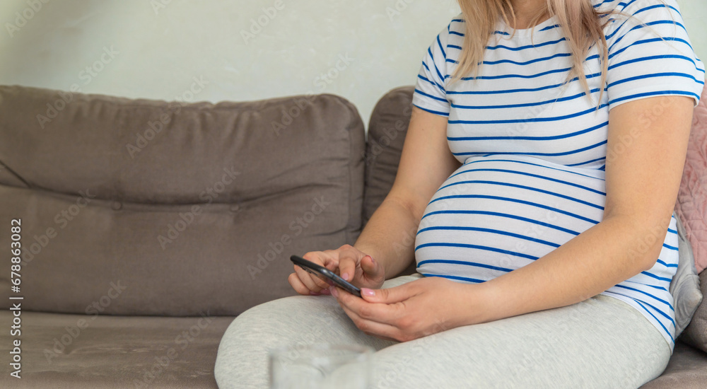 A pregnant woman plays on the phone on the Internet. Selective focus.
