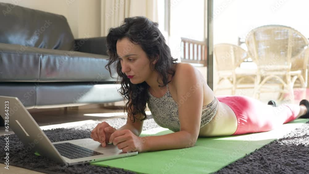 Hispanic woman lying on the floor with a laptop wearing sports clothing in the living room of her home Hispanic woman lying on the floor with a laptop wearing sports clothing in the living room of her home