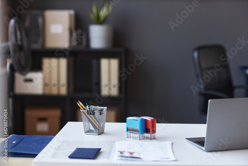 Workplace of white collar worker with laptop, stamps for documents and other supplies on desk standing in front of camera in coworking space