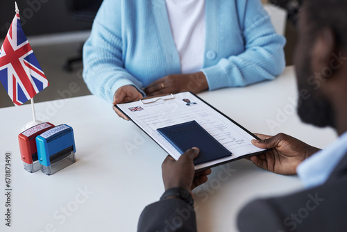 Young African American female manager of visa application center passing documents to male applicant over desk after approving