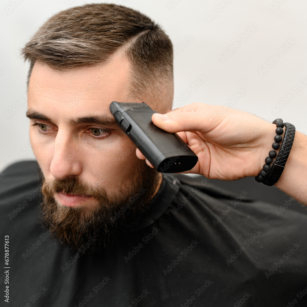 Barber shaves the temple with cordless trimmer during a short haircut on the sides of the head. Barber shaves the temple with cordless trimmer during a short haircut on the sides of the head.