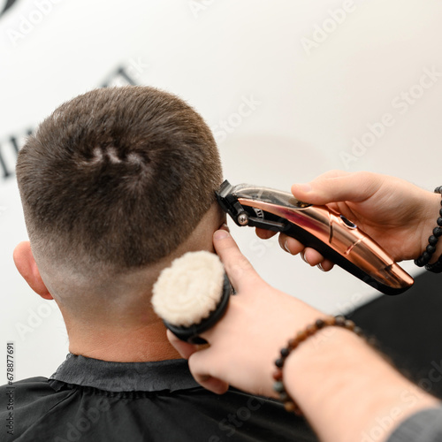 Barber shaves the contour of the oval line with a clipper on the client head. A man with a beard gets a haircut in a barbershop chair.