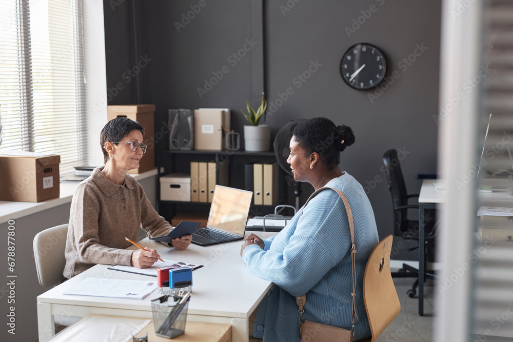 Young African American female applicant answering questions of manager working in visa application center during conversation in office Young African American female applicant answering questions of manager working in visa application center during conversation in office