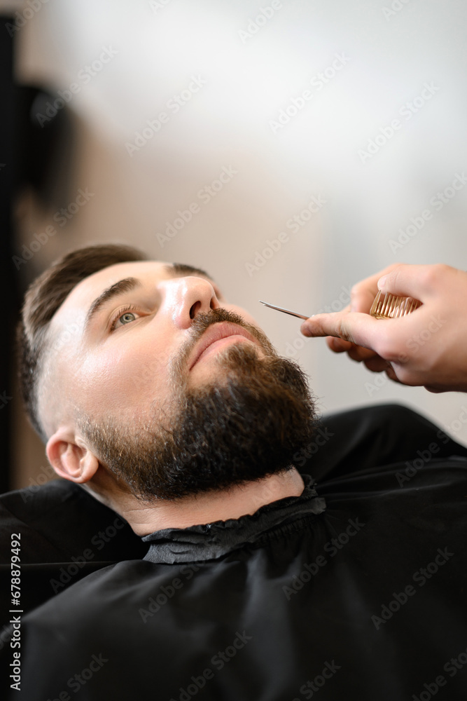 Fototapeta premium A barber stylist trims a Caucasian mans mustache with scissors