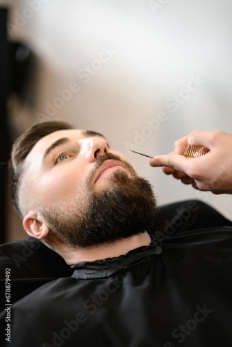 A barber stylist trims a Caucasian mans mustache with scissors