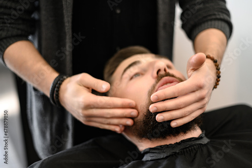 A barber massages and rubs a male client beard after applying moisturizing oil photo