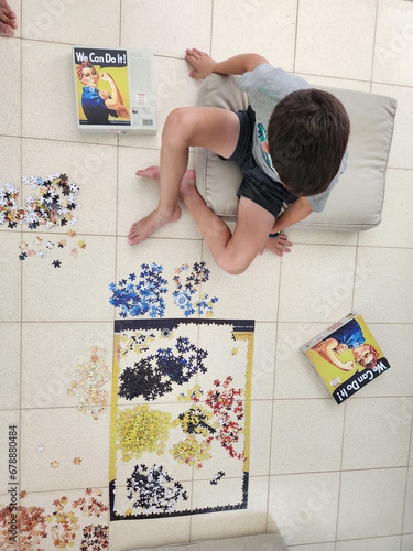 Boy playing jigsaw puzzle game at home, top view from above