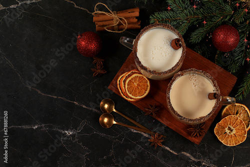 Eggnog with cinnamon, nutmeg and ginger milk drink for Christmas and winter holidays on a background of fir branches and decorations. Warming milk drink during the cold season, holiday composition,
