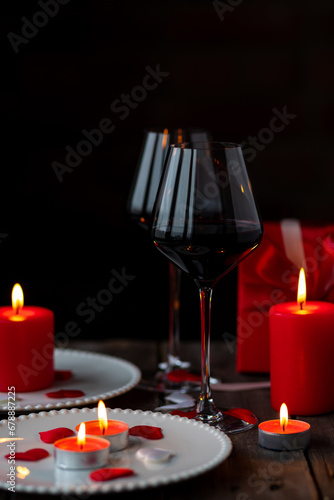 Saint Valentine's Day celebration. Red burning candles, hearts, gift box, postcard on dark wooden background. Happy holiday . Table decor for festive dinner, romantic atmosphere. Copy space for text