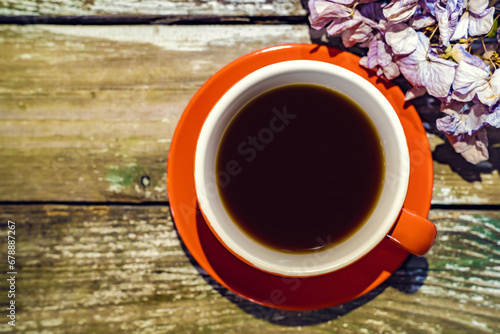 Orange mug of coffee, dry hydrangea. Wooden aged background.