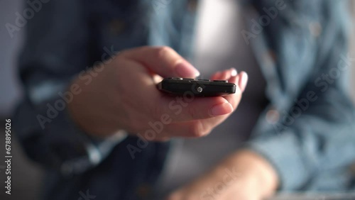 Close-up of female hands holding a TV remote control. Hand pressing remote control. Watching TV photo