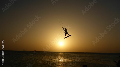 Silhouette of a person kitesurfing in the sea with the bright golden sunset in the background