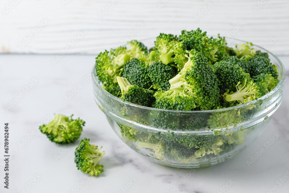 Glass bowl of fresh raw organic broccoli close-up on a marble kitchen table in a light background Glass bowl of fresh raw organic broccoli close-up on a marble kitchen table in a light background