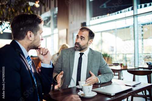 Mature businessman mentoring younger colleague in cafe meeting photo