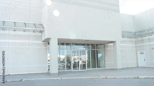 vacant generic empty store storefront beige white clean with no sign or logo with pillars and glass doors below with reflection of parking lot with lens flare and car vehicle passing in front photo