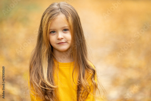 Portrait of a beautiful little blonde girl in a yellow dress in an autumn park.