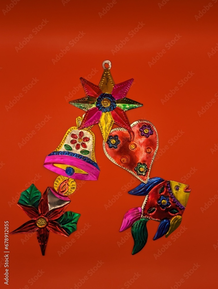 Mexican tin christmas decorations in christmas tree shape, red background, centered. Fish, star, poinsettia, bell, heart
