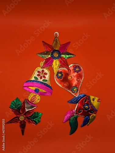 Mexican tin christmas decorations in christmas tree shape, red background, centered. Fish, star, poinsettia, bell, heart