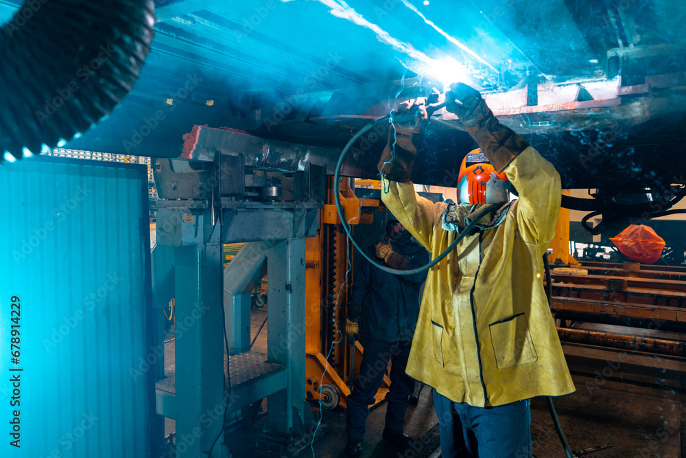 man working under a train using a welder  - obrazy, fototapety, plakaty 