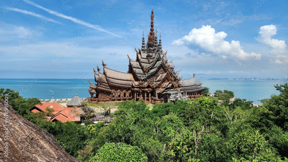 Scenic wooden Temple of Truth in Pattaya surrounded by trees and a sea on a sunny day