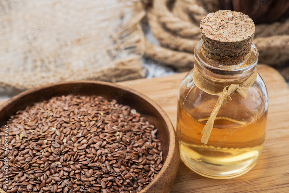Flaxseed oil in a bottle with brown flax seeds in a wooden bowl close-up.