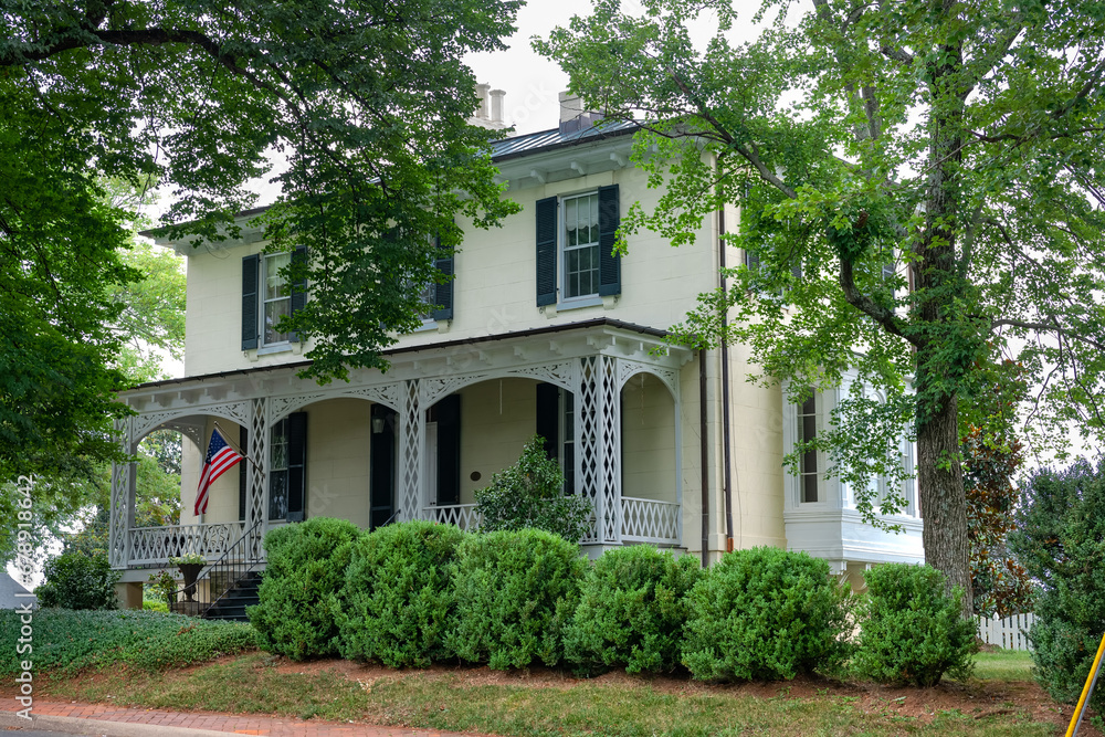 traditional American two-story house with a veranda and lawn at the entrance.