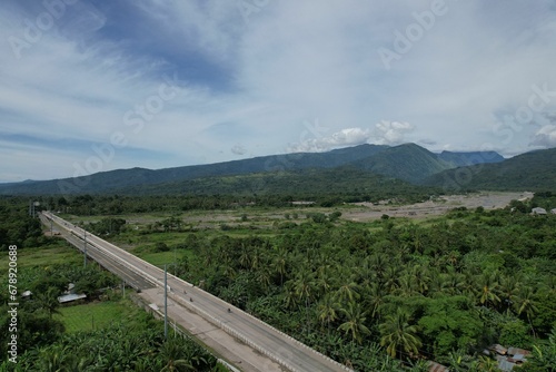 Drone view of a landscape scene with mountains surrounded by various trees and fields near a highway