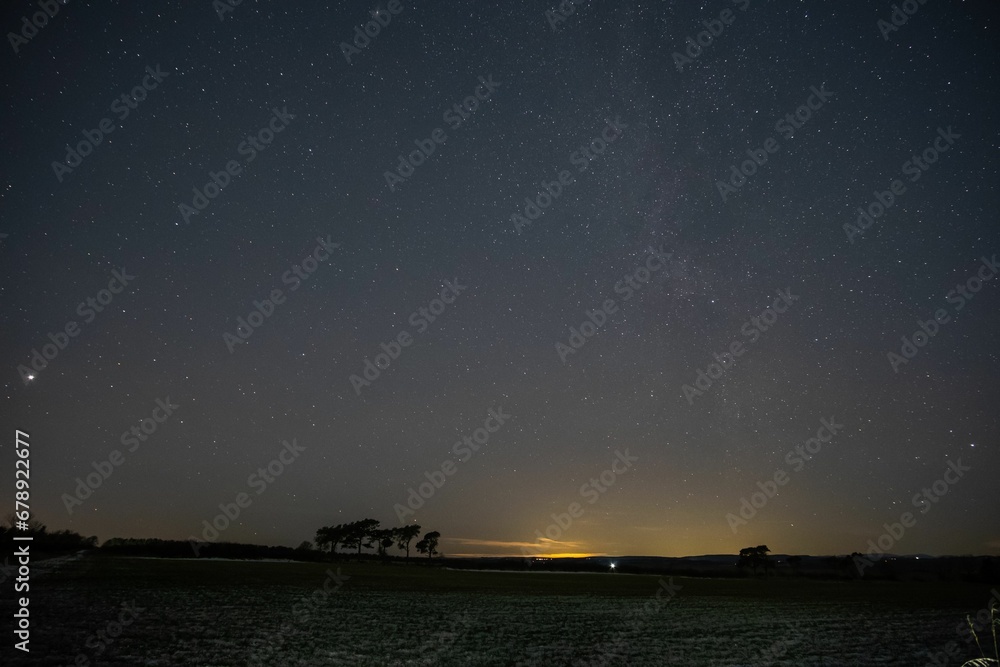 Night view of a barren field with silhouette of trees in the background under a starry night