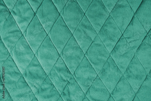 Quilted velours fabric background. Green texture blanket or puffer jacket, stiched with diamond pattern, soft wrinkled surface, crupmed textile photo