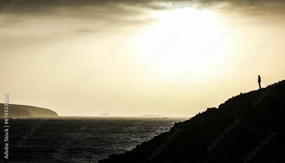 Silhouette shot of a person standing on the sloping side of a mountain overlooking the sea