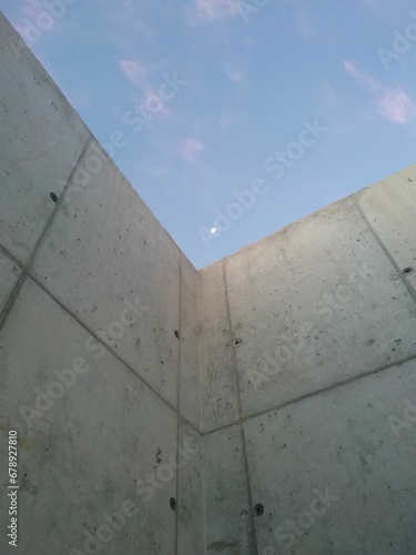 Vertical shot of a wall with the moon visible in the sky during the afternoon