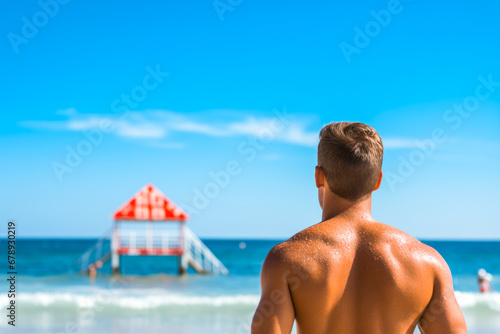 Rear view of a male lifeguard who dutifully watches over swimmers ready to take immediate action in case of a life threatening situation in the ocean photo