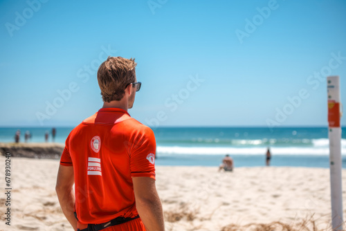 Rear view of a male lifeguard who dutifully watches over swimmers ready to take immediate action in case of a life threatening situation in the ocean photo