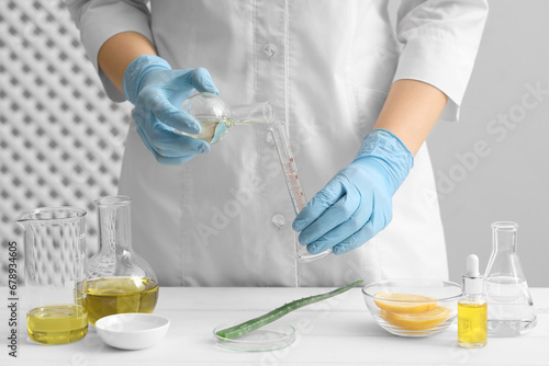 Scientist developing cosmetic oil at white table, closeup