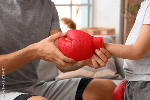 Young man and his little son with boxing glove at home, closeup