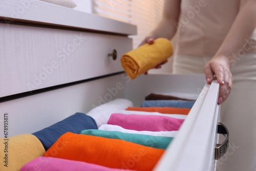 Woman putting rolled shirt into drawer at home, closeup. Organizing clothes