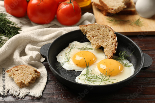 Delicious fried eggs served with bread and tomatoes on wooden table