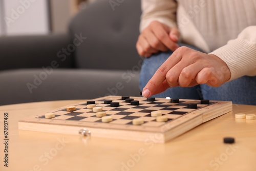 Woman playing checkers at wooden table indoors, closeup