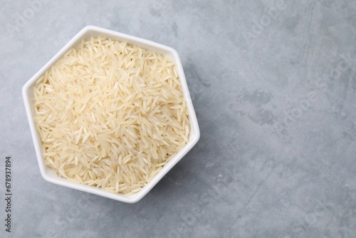 Raw rice in bowl on light grey table, top view. Space for text