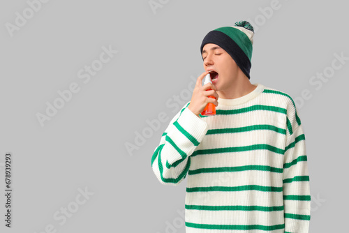Ill young man spraying his sore throat on light background