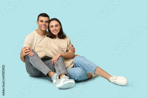 Cheerful young couple sitting on floor and hugging on blue background