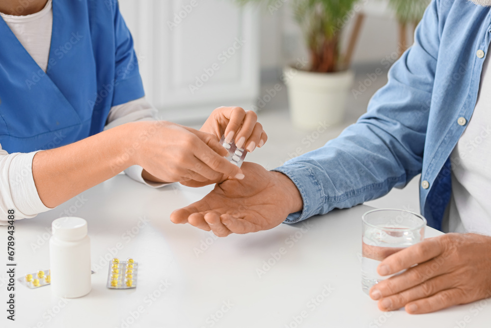 Senior man with nurse taking pills in kitchen, closeup