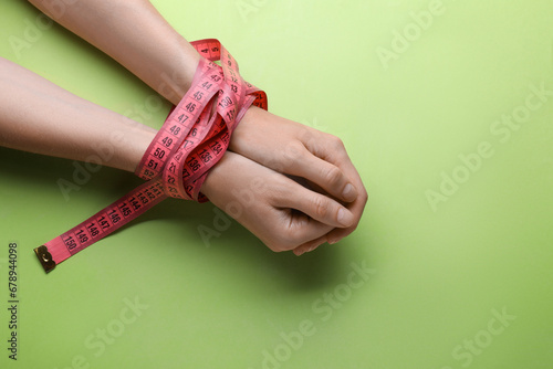 Woman tied with measuring tape on light green background, top view. Diet concept