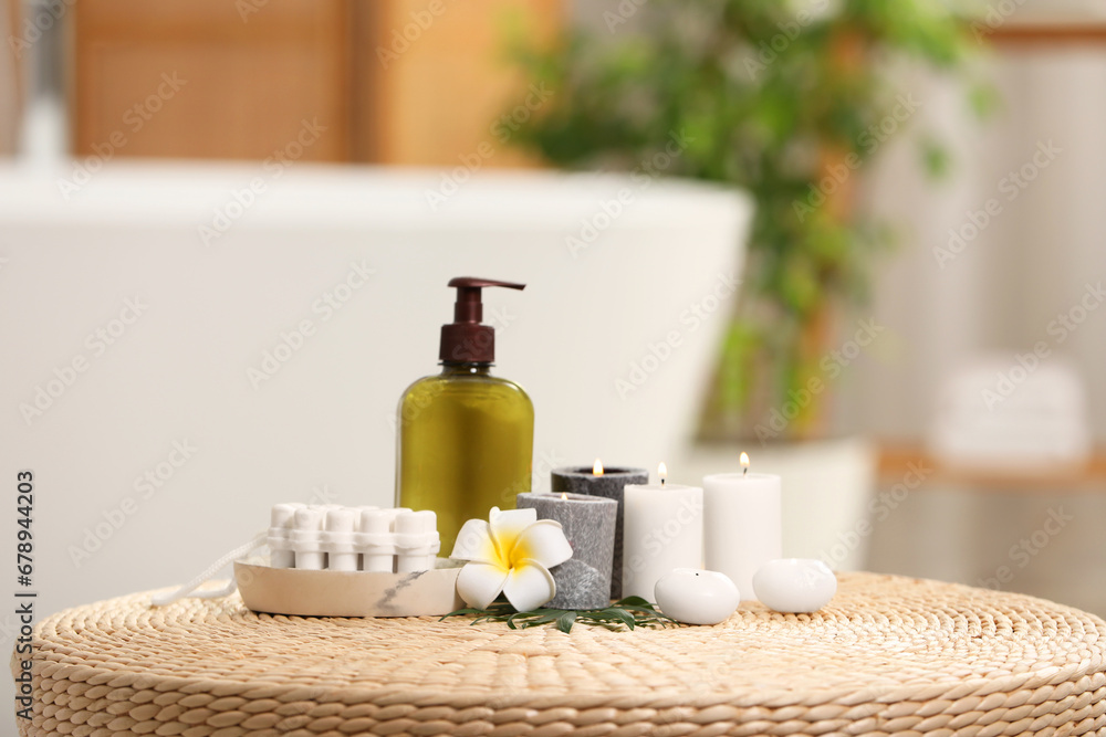 Spa products, burning candles and plumeria flower on wicker table in bathroom