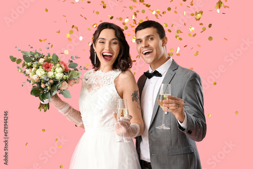 Young wedding couple with bouquet of flowers and champagne on pink background photo