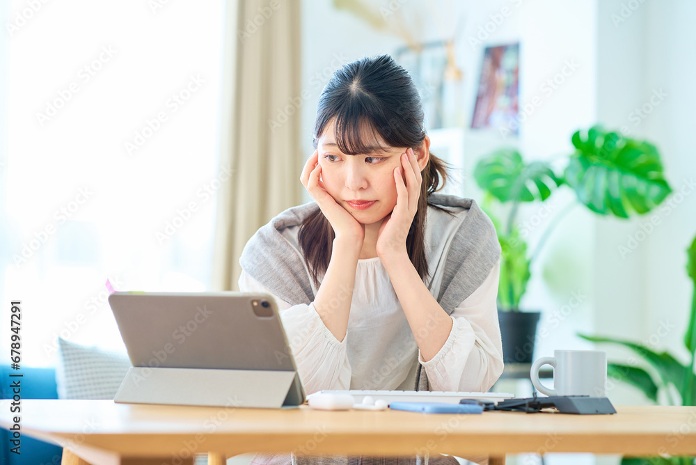 部屋でパソコン作業をしながら疲れた表情の若い女性 部屋でパソコン作業をしながら疲れた表情の若い女性