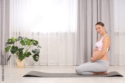 Pregnant woman sitting on yoga mat at home