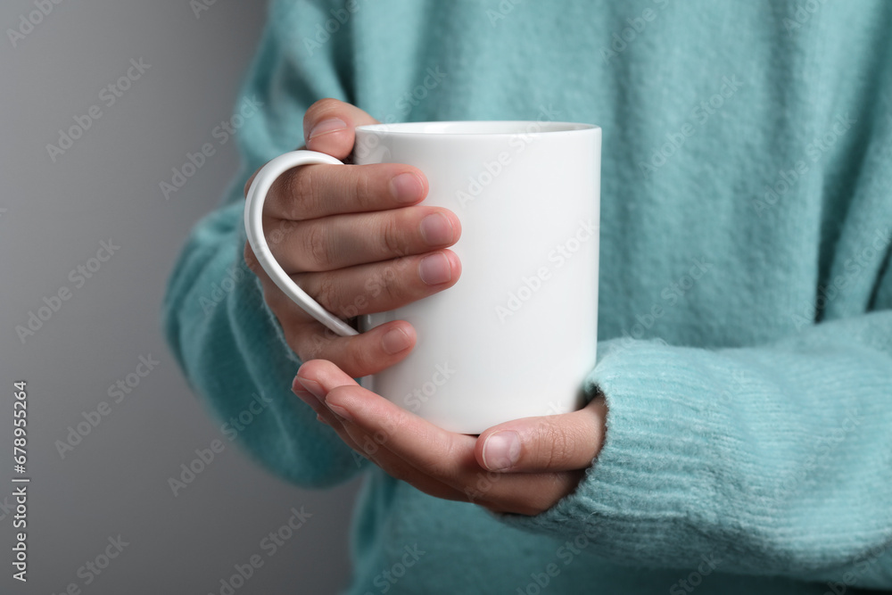 Woman holding white mug on gray background, closeup Woman holding white mug on gray background, closeup