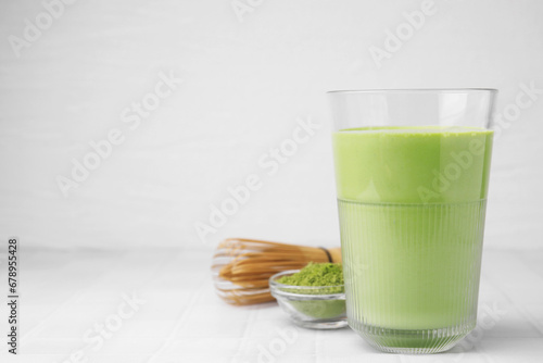 Glass of tasty matcha smoothie, powder and bamboo whisk on white tiled table, space for text